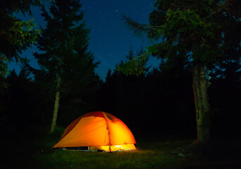 Orange illuminated tent in dark night forest with night sky and stars © Pavlo Vakhrushev