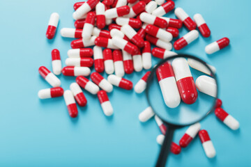 A handful of Red and white pill capsules are examined with a magnifying glass on a blue background