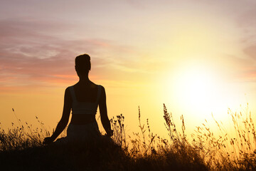 Silhouette of woman meditating outdoors at sunset, back view. Space for text