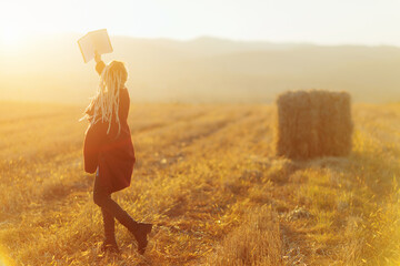 Cheerful young woman reads a book in the rural field