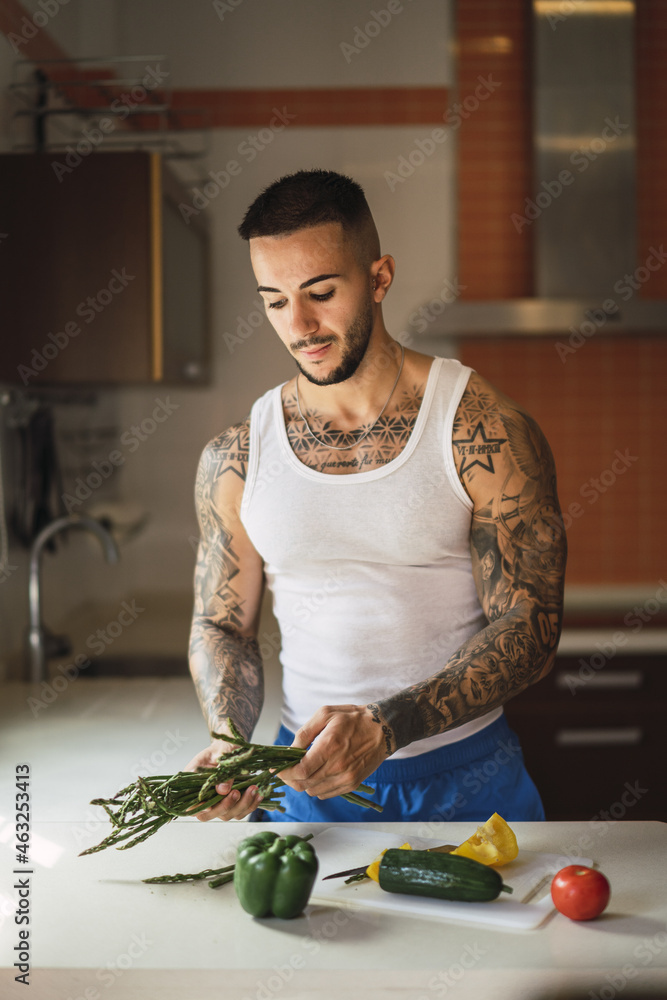 Sticker Vertical shot of a tattooed Caucasian male athlete preparing healthy food in the kitchen