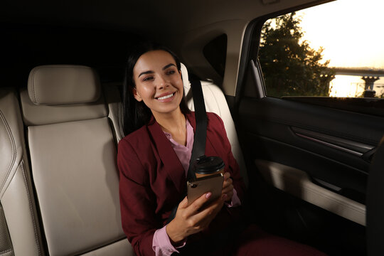 Young woman with smartphone and cup of drink in modern taxi