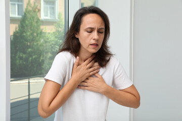 Mature woman suffering from breathing problem near window indoors - obrazy, fototapety, plakaty