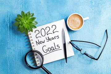 New year goals 2022 on desk. 2022 goals with notebook, coffee cup and eyeglasses on blue background. Resolutions, plan, strategy, action, idea concept