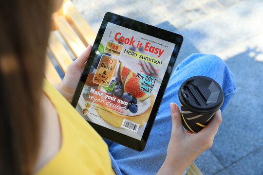 Woman with coffee reading online magazine on tablet outdoors, closeup