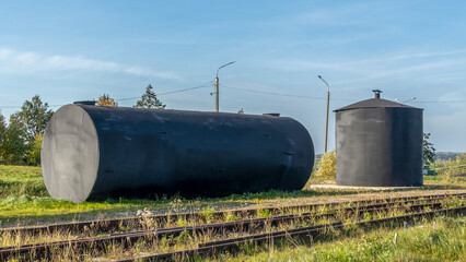 Obraz premium A metal fuel tank in an antique railway yard. Old black Fuel Tank on the village railroad station.