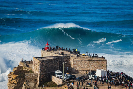 Surfer riding huge wave near the Fort of Sao Miguel Arcanjo Lighthouse in Nazare, Portugal. Nazare is famously known for having the biggest waves in the world.