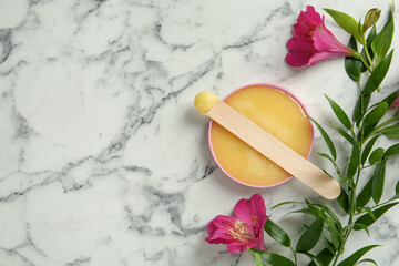 Spatula with wax and flowers on white marble table, flat lay. Space for text