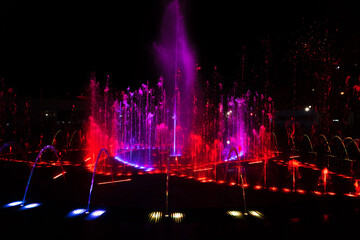 Fototapeta na wymiar Red-pink jets of the fountain at night.