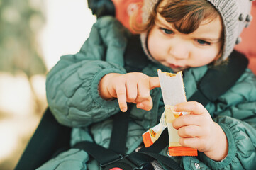 Happy toddler kid eating fruit bar, healthy snack, sitting in stroller