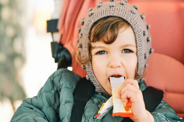 Happy toddler kid eating fruit bar, healthy snack, sitting in stroller