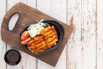 Japanese deep fried pork cutlet or Tonkatsu with sauce, cabbage and tomato in black ceramic plate on old wood cutting board on white wooden texture background with copy space for text, top table view