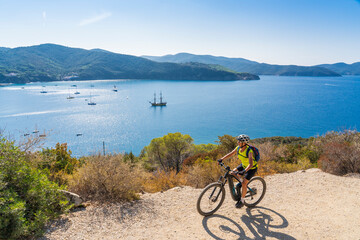 nice woman riding her electric mountain bike on the coastline above the mediterranean sea on the Island of Elba in the tuscan Archipelago, Tuscany, Italy
