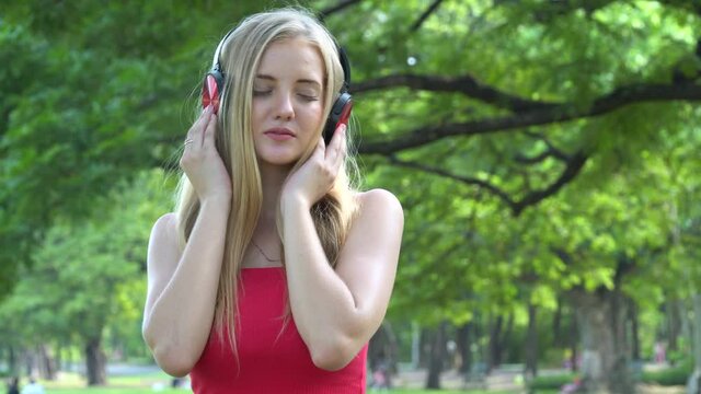 happy Beautiful young woman in red shirt listening to music with headphones enjoy in nature park outdoors .