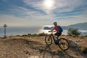 nice woman riding her electric mountain bike at sunset at the coastline of mediterranean sea on the...
