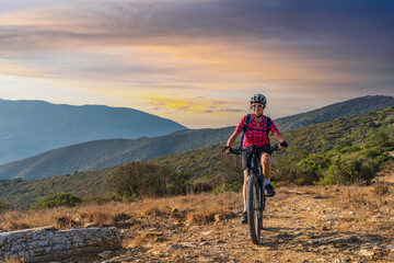 Naklejka premium nice woman riding her electric mountain bike at sunset at the coastline of mediterranean sea on the Island of Elba in the tuscan Archipelago Tuscany, Italy
