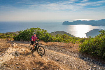 nice woman riding her electric mountain bike at the coastline of mediterranean sea on the Island of...