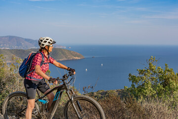nice woman riding her electric mountain bike at the coastline of mediterranean sea on the Island of Elba in the tuscan Archipelago Tuscany, Italy
