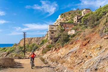 Fototapeta premium nice active woman riding her electric mountain bike in the abandoned Iron Ore mines of Calamite peninsula on the Island of Elba, Tuscan Archipelago, Tuscany,Italy 