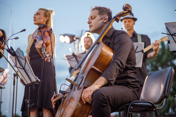 Male cellist playing in orchestra at outdoor concert - obrazy, fototapety, plakaty
