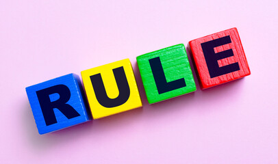 On a light pink background, multi-colored wooden cubes with the text RULE