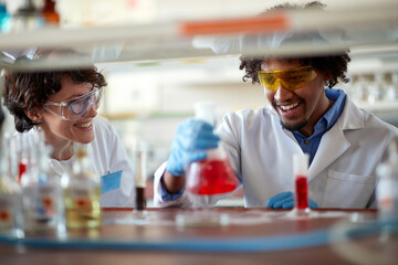 Young colleagues in a protective gear are in a good mood while work with colorful chemicals in the university laboratory. Science, chemistry, lab, people