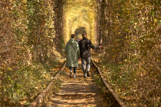 A loving couple view from the back. A place for dating. A romantic walk outside the city. Out-of-town entertainment. Walk on the railroad. Tunnel of love. Beautiful autumn. Natural arch made of trees.