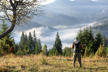 Tourist with backpack in mountains on sunny day, back view. Space for text