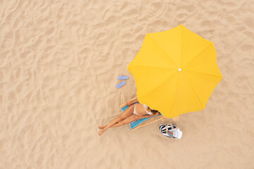 Woman resting in sunbed under yellow beach umbrella at sandy coast, aerial view. Space for text