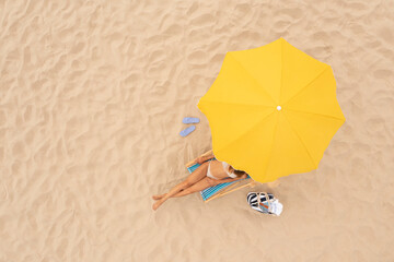 Woman resting in sunbed under yellow beach umbrella at sandy coast, aerial view. Space for text © New Africa
