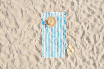 Striped beach towel, straw hat and flip flops on sand, aerial view
