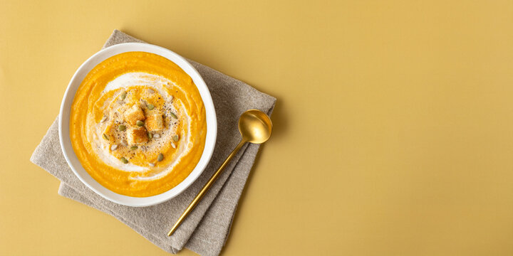 Pumpkin soup with toast and seeds on a beige background isolated banner. Autumn vegetables, healthy food.