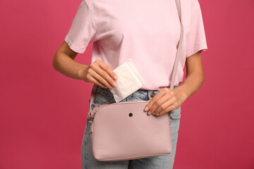 Fototapeta na wymiar Young woman putting menstrual pad into purse on bright pink background, closeup