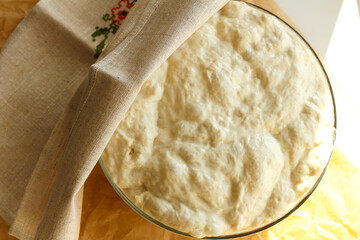 Ciabatta yeast dough rests and rises in a glass bowl under a towel