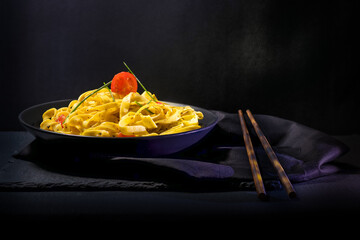 Plato de pasta italiana de tallarines con tomate, cubiertos de palillos y con fondo negro