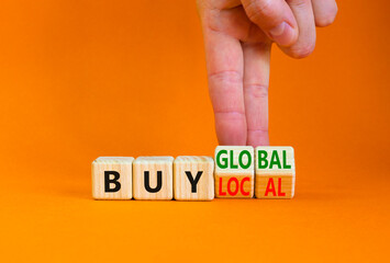 Buy local or global symbol. Businessman turns wooden cubes, changes words 'buy local' to 'buy global'. Beautiful orange table, orange background. Business, buy local or global concept. Copy space.