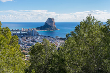 View of pine trees the blue Mediterranean Sea and the urban architecture of the coastal city of Calpe travel destination in Spain 