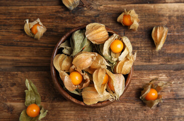 Ripe physalis fruits with dry husk on wooden table, flat lay