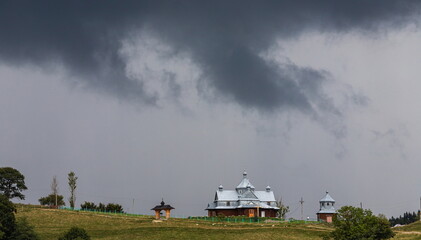 Obraz na płótnie Canvas Storm clouds, ominous sky, hill and church, green trees before the rain