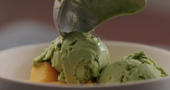 Slow motion add green ice cream in white bowl with ripe mango