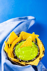 Guacamole sauce and nachos chips on a blue background. Guacamole bowl with tortilla chips with a...