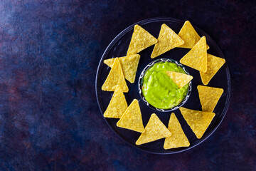 Guacamole sauce and nachos chips on dark background. Guacamole bowl with tortilla chips. Copy...