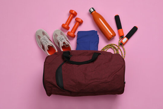 Gym bag and sports equipment on light pink background, flat lay