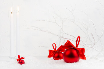 Traditional christmas background with white burning candles, rich red decorations - balls with satin ribbons, bows in white snow in soft light fairy winter forest with frosty branches, copy space.