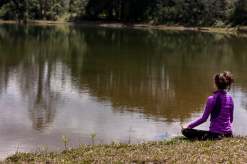 Woman sitting on her back meditating in front of a pond with Cloud reflections in the water.
