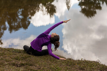 Woman exercising yoga outdoors in front of a pond with Cloud Reflections in the water.