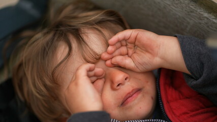 Fototapeta premium Upset tired baby toddler rubbing face with hand, tearful sad exhausted child