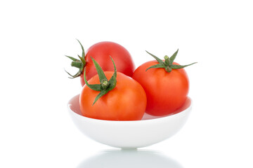Three red organic tomatoes with a white ceramic saucer, close-up, isolated on white.