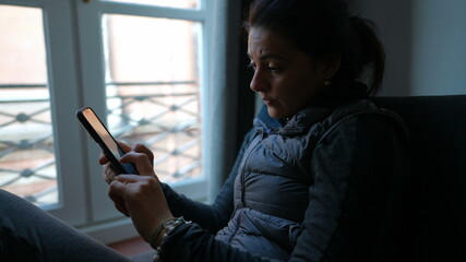 Woman using smartphone at home typing message with concerned emotion