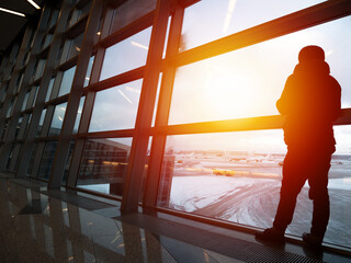 Fototapeta na wymiar Silhouette of unrecognizable man waiting the flight in airport departure terminal